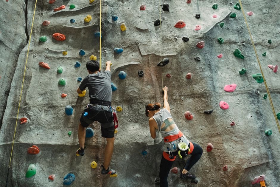 Kopiantys žmonės su apraišais ant dirbtinės sienelės sporto salėje