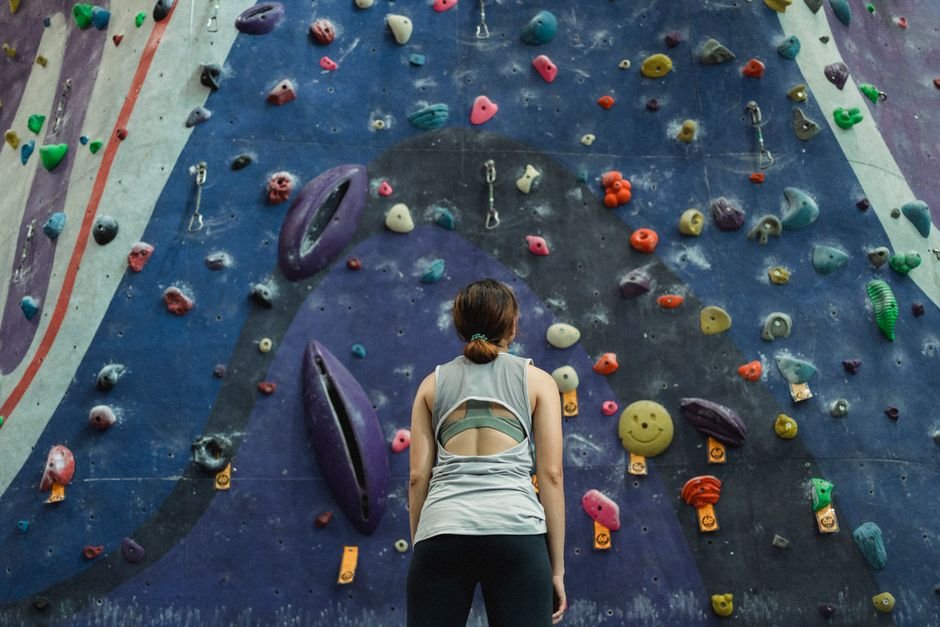 Jauna sportininkė žvelgia į ryškiaspalvę laipiojimo sienelę sporto salėje